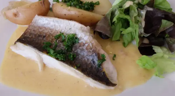Filet de mulet poisson, servi avec des pommes de terre rôties, une salade verte et une sauce crémeuse.