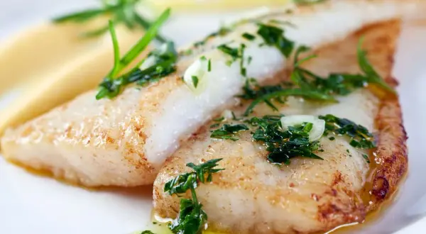Deux filets de poisson maigre, dorés et garnis d'herbes fraîches, reposent sur une purée crémeuse. Un délice simple et savoureux.