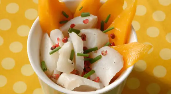 Délicieuse recette cabillaud enfant : morceaux de poisson blanc, mangue fraîche, ciboulette et poivre rose dans un bol.