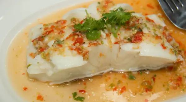 Filet de poisson blanc nappé d'une sauce épicée aux herbes et piments, rappelant un beurre blanc revisité.