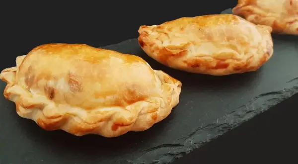 Trois chaussons dorés, un pastel thon savoureux, sur une ardoise sombre.