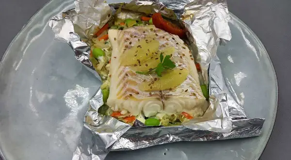 Un délicieux filet d'églefin en papillote, garni de légumes croquants et de fines tranches d'agrumes, prêt à être dégusté.
