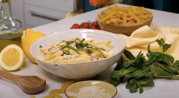 Un plat de pâtes au thon crémeuses, garni de menthe fraîche et de zeste de citron, prêt à être dégusté.
