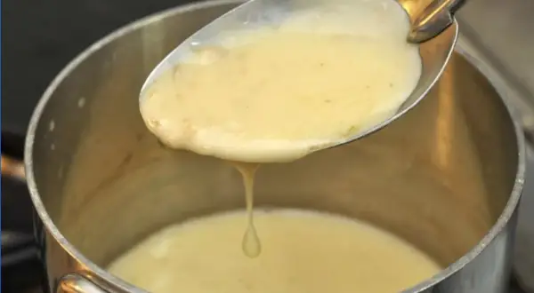 Une cuillère de sauce onctueuse, peut-être un beurre nantais, s'écoule dans une casserole.