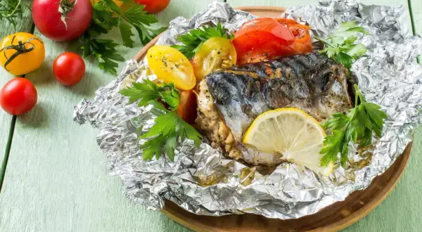 Poisson en papillote, un maquereau cuit avec des tomates et du persil, garni d'une tranche de citron.