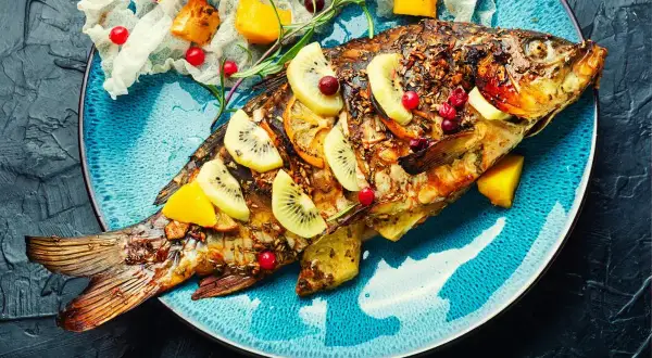 Poisson entier rôti, garni de tranches de kiwi, d'orange et de canneberges. Une belle recette poisson pour un repas festif.
