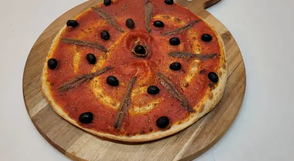 Pizza à la sauce tomate, olives noires et anchois, prête à être dégustée. Une recette simple et savoureuse.