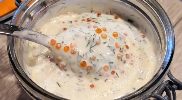 Une cuillère de sauce pour saumon crémeuse, parsemée d'aneth et de perles d'œufs de poisson, dans un bocal en verre.
