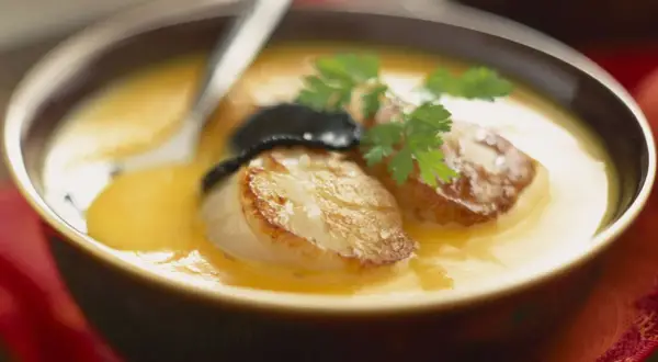 Velouté de butternut avec saint jacques poêlées, garni de persil et d'une touche de truffe.