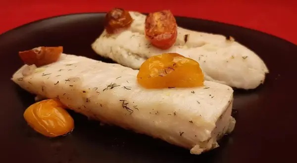 Deux filets de merlu au four, tendres et savoureux, ornés de tomates cerises rôties et d'aneth frais. Un délice simple et sain.