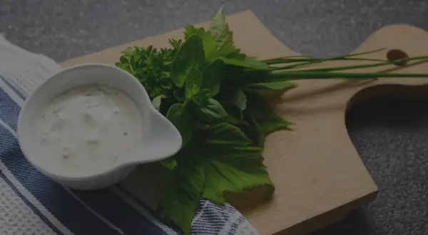 Un bol de sauce tartare crémeuse, garni d'herbes fraîches sur une planche en bois.
