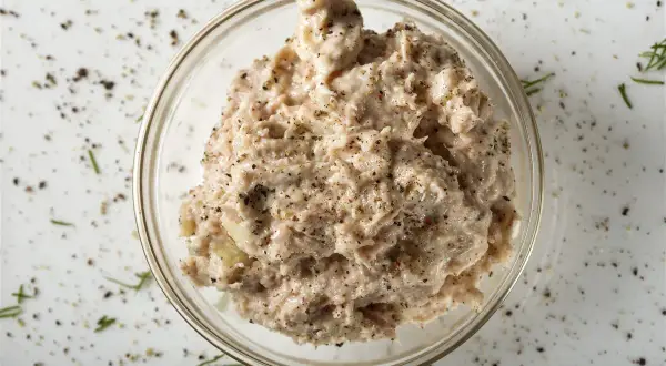 Un bol de rillettes de thon, assaisonnées de poivre noir et d'herbes, prêt à être dégusté.
