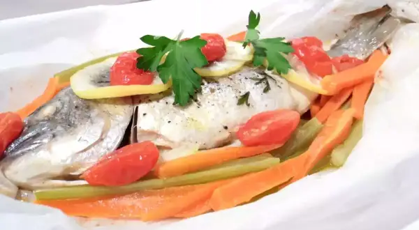 Dorade au four en papillote, garnie de tomates cerises, rondelles de citron, carottes et persil. Un plat sain et savoureux.