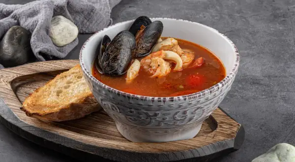 Bol de soupe de poisson aux moules et crevettes, servi avec une tranche de pain grillé et une touche de sauce rouille.
