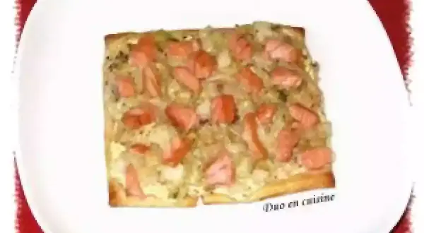 Tarte rectangulaire garnie de poireaux et de morceaux de saumon fumé, servie sur une assiette blanche.