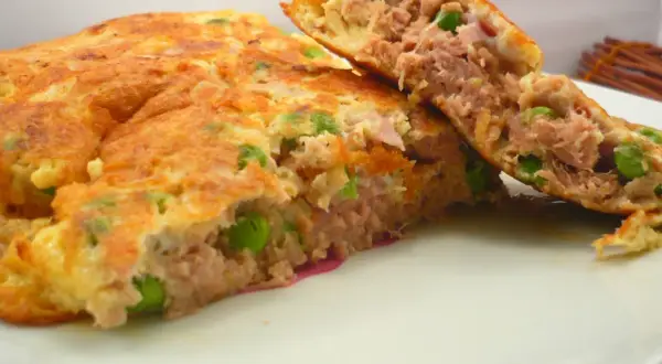 Une savoureuse omelette au thon et petits pois, coupée en deux pour révéler sa garniture généreuse. Un délice simple et rapide.