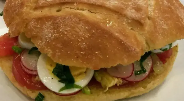 Un délicieux pan bagnat garni de tomates, œufs durs, radis et herbes fraîches. Parfait pour une recette facile et savoureuse.