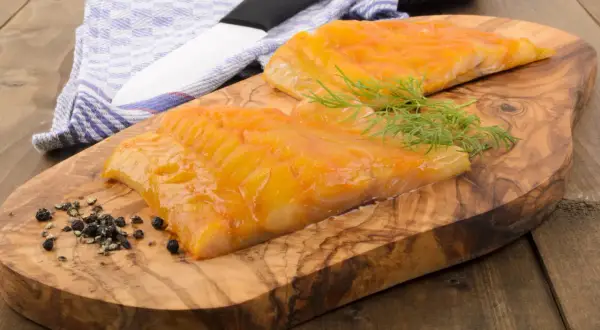 Deux beaux filets de haddock poisson fumé, prêts à être dégustés, sur une planche en bois d'olivier avec de l'aneth et du poivre.