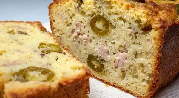 Tranche d'un cake au thon moelleux, garni d'olives vertes et de morceaux de thon. Parfait pour un apéritif ou un repas léger.