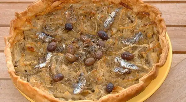 Pissaladière garnie d'anchois et d'olives, sur une pâte brisée ou feuilletée dorée.