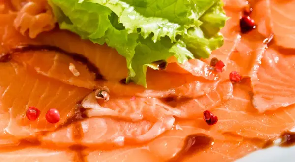 Délicieux carpaccio de saumon, fines tranches de poisson cru, garnies de quelques baies roses et d'une feuille de laitue croquante.