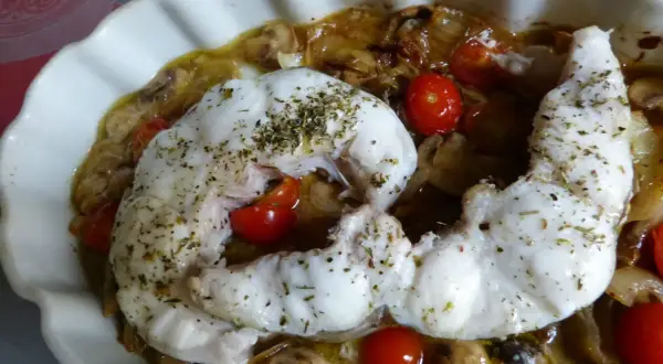 Un délicieux filet de congre au four, parsemé d'herbes, servi avec des tomates cerises et des champignons dans un plat blanc ondulé.