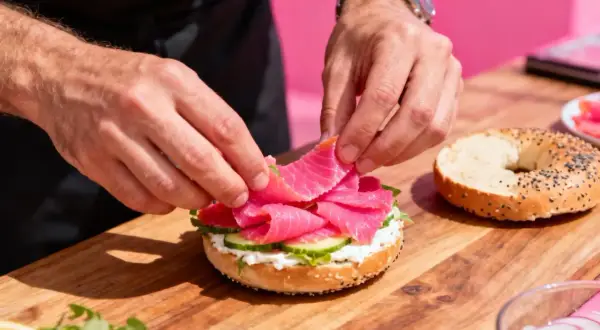 Préparation d'un bagel saumon frais avec des tranches de concombre et de la crème onctueuse.