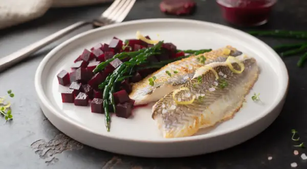 Deux filets de limande cardine poêlés, servis avec des dés de betterave et de la salicorne, garni de zestes de citron et de pousses vertes.
