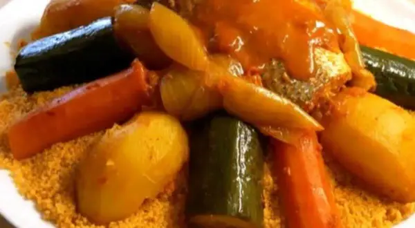Un plat généreux de couscous garni de poisson, carottes, courgettes et pommes de terre, le tout nappé d'une sauce savoureuse.