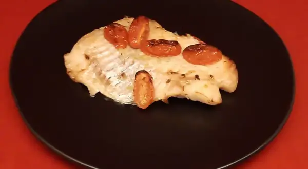 Un filet de dorade sebaste cuit, garni de tomates cerises rôties, servi sur une assiette noire.