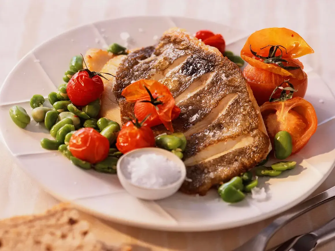 Filet de saint pierre grillé, servi avec des tomates cerises rôties et des fèves, un délice simple et savoureux.