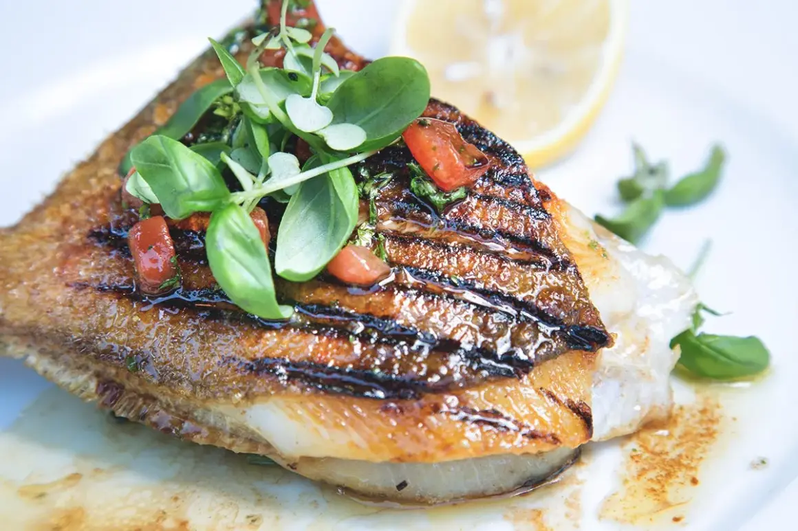 Un délicieux saint pierre poisson grillé, garni de tomates et de basilic frais, servi avec un quartier de citron.