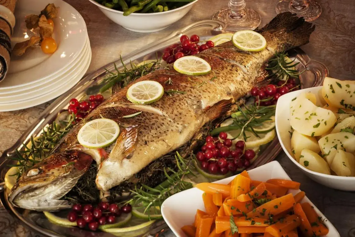 Un poisson entier, un turbot, est servi sur un plateau avec des rondelles de citron, des airelles et du romarin. Des pommes de terre et des carottes sont disposées sur les côtés.