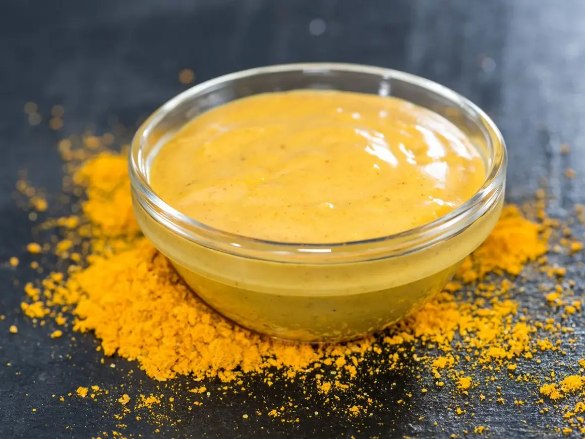 Un bol de sauce pour poisson, d'une belle couleur jaune, est posé sur un lit de poudre d'épices.