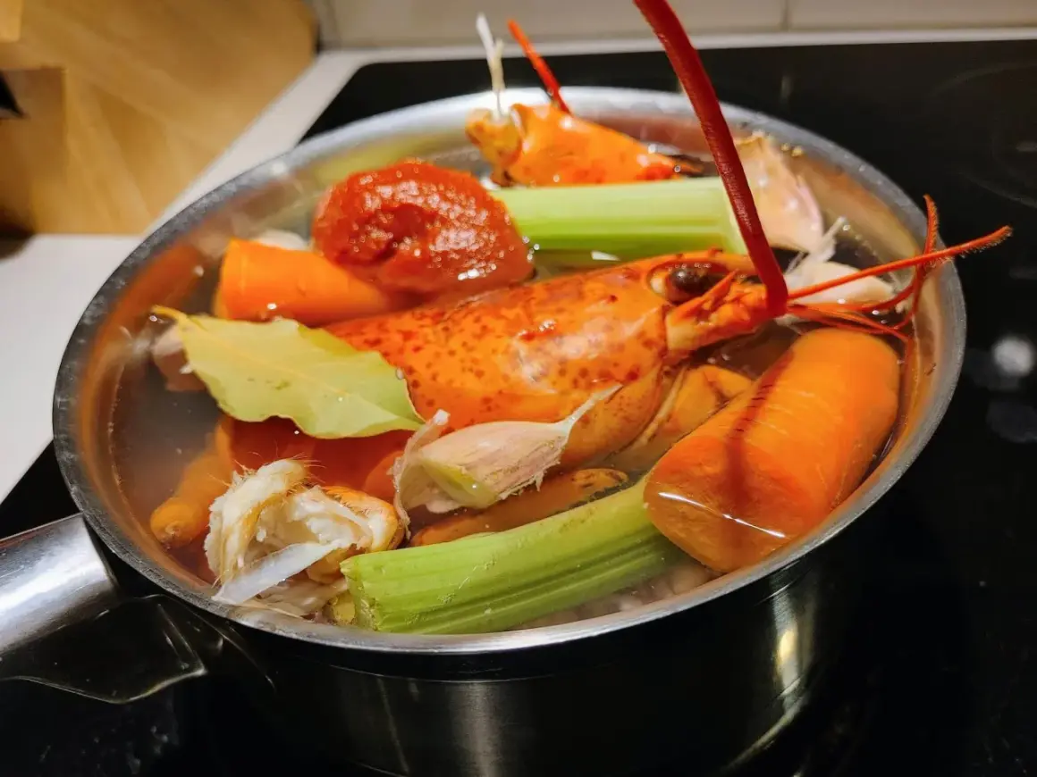 Deux homards entiers mijotent dans un court-bouillon avec carottes, céleri, ail et feuille de laurier.