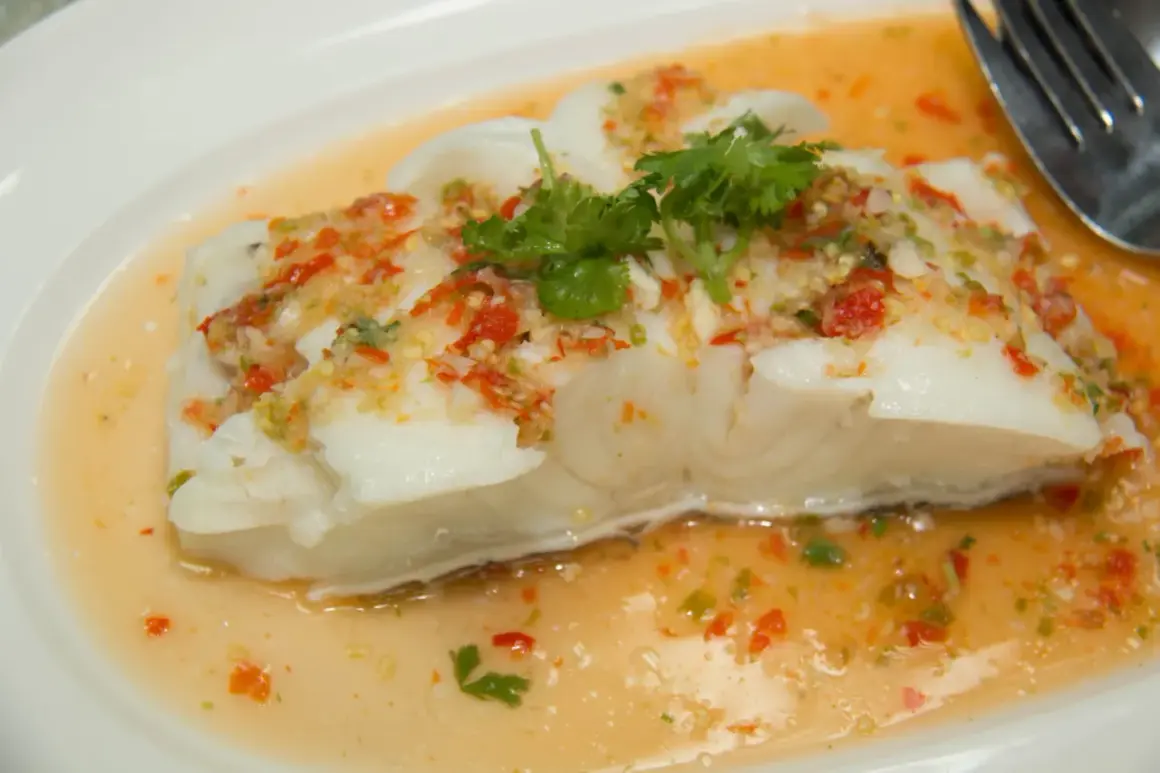 Filet de poisson blanc nappé d'une sauce épicée aux herbes et piments, rappelant un beurre blanc revisité.
