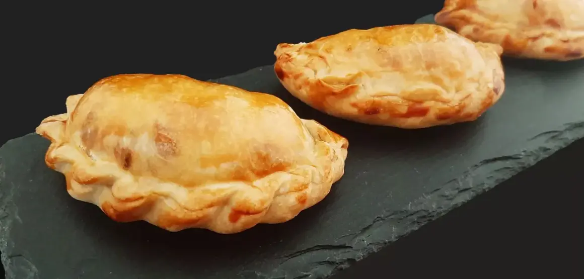 Trois chaussons dorés, un pastel thon savoureux, sur une ardoise sombre.