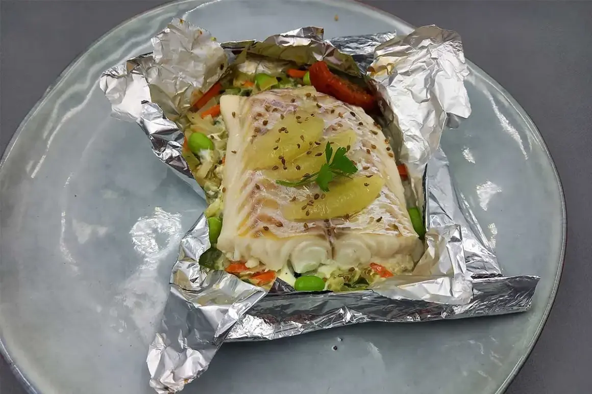 Un délicieux filet d'églefin en papillote, garni de légumes croquants et de fines tranches d'agrumes, prêt à être dégusté.
