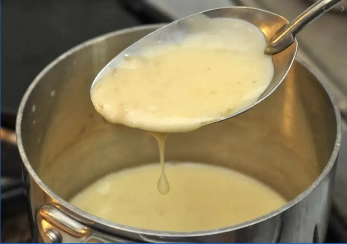 Une cuillère de sauce onctueuse, peut-être un beurre nantais, s'écoule dans une casserole.
