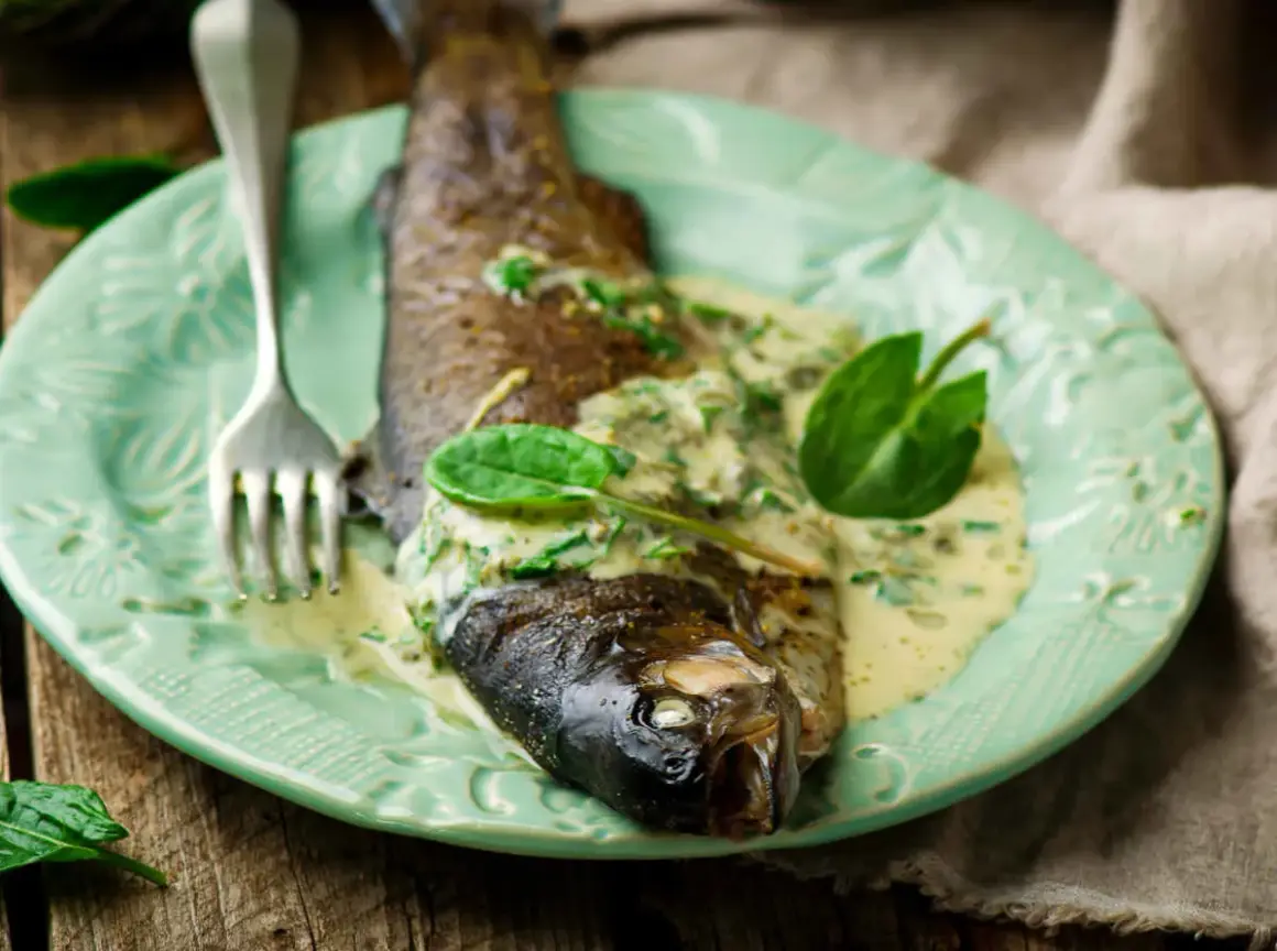 Poisson entier nappé d'une onctueuse sauce à l'oseille, garni de feuilles vertes fraîches, sur une assiette menthe.