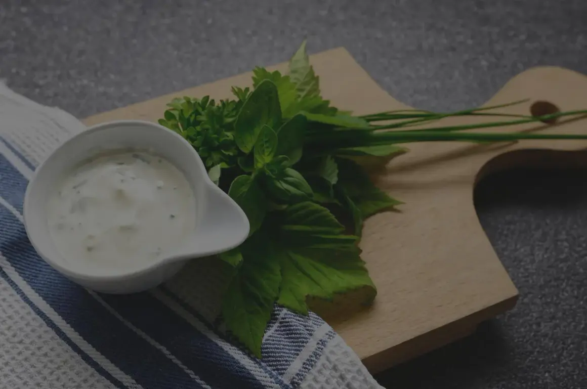 Un bol de sauce tartare crémeuse, garni d'herbes fraîches sur une planche en bois.