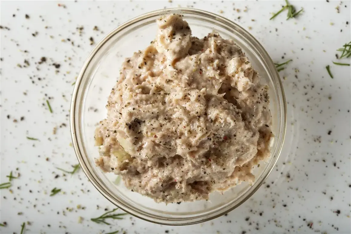 Un bol de rillettes de thon, assaisonnées de poivre noir et d'herbes, prêt à être dégusté.