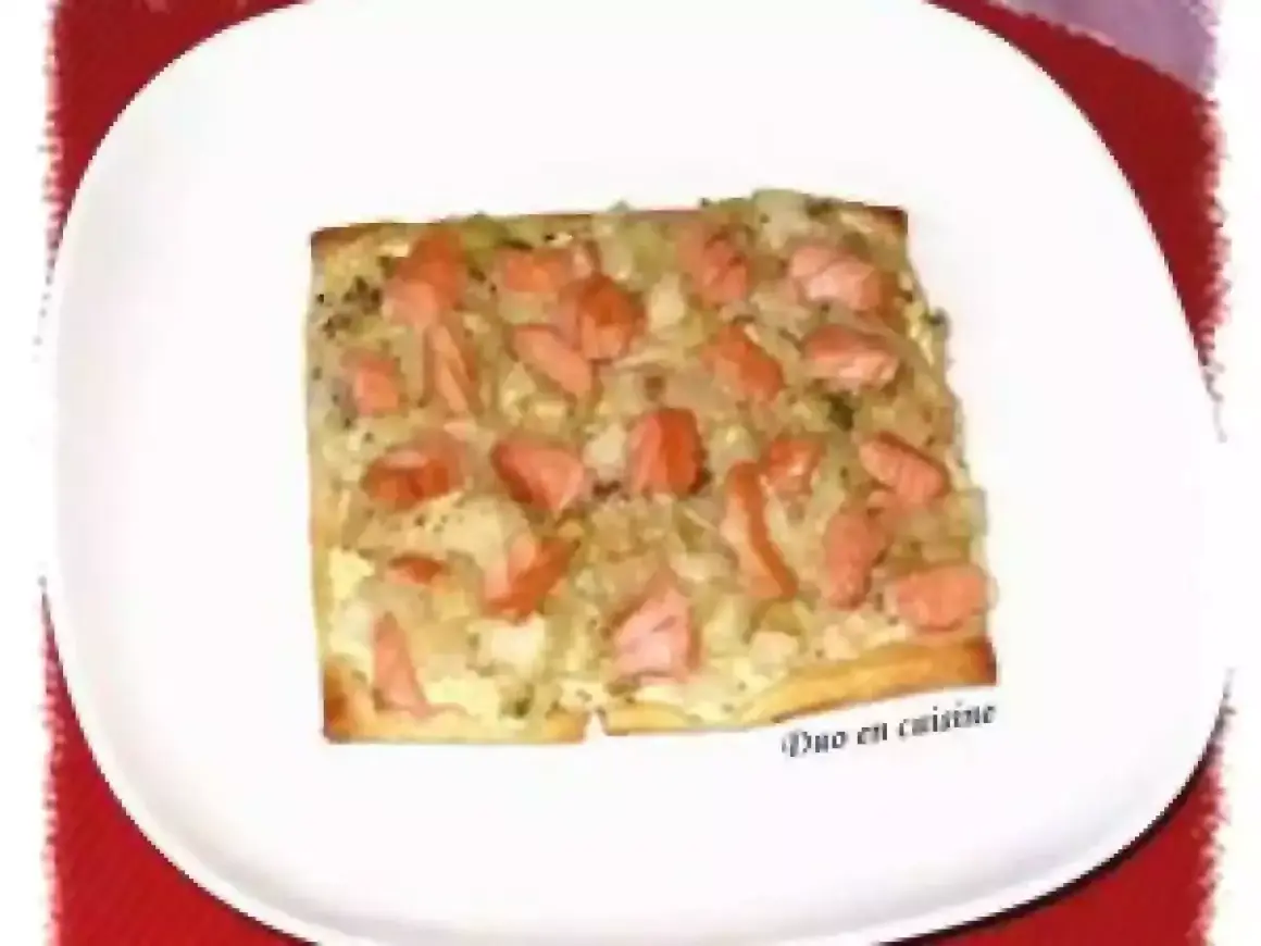 Tarte rectangulaire garnie de poireaux et de morceaux de saumon fumé, servie sur une assiette blanche.