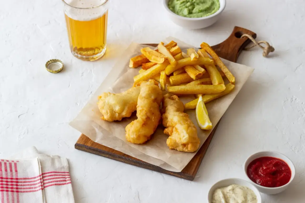 Un plateau de fish and chips croustillant avec des frites dorées, un quartier de citron, de la sauce tartare, de la purée de petits pois et une bière fraîche.