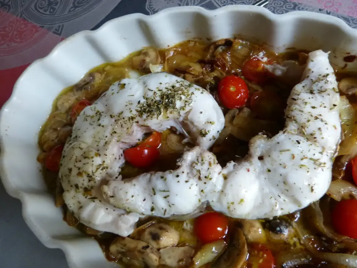 Un délicieux filet de congre au four, parsemé d'herbes, servi avec des tomates cerises et des champignons dans un plat blanc ondulé.