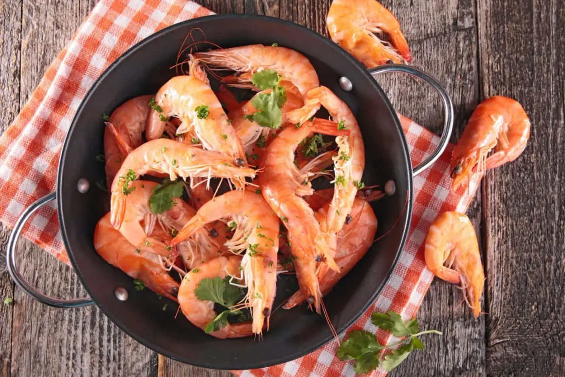 Un plat de crevettes grises fraîchement cuites, garnies de persil, sur une nappe à carreaux orange et blanche.