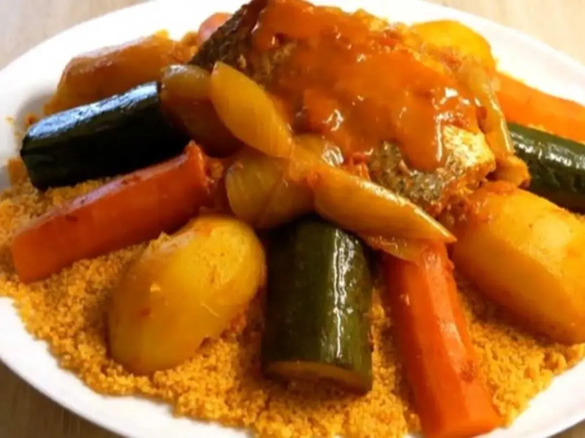 Un plat généreux de couscous garni de poisson, carottes, courgettes et pommes de terre, le tout nappé d'une sauce savoureuse.
