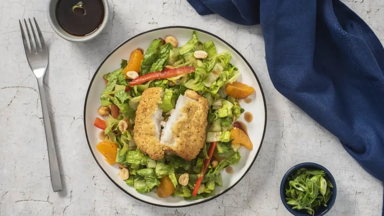 Une salade fra&icirc;che et color&eacute;e avec un poisson pan&eacute; croustillant, des quartiers d'orange, des poivrons rouges et des cacahu&egrave;tes.