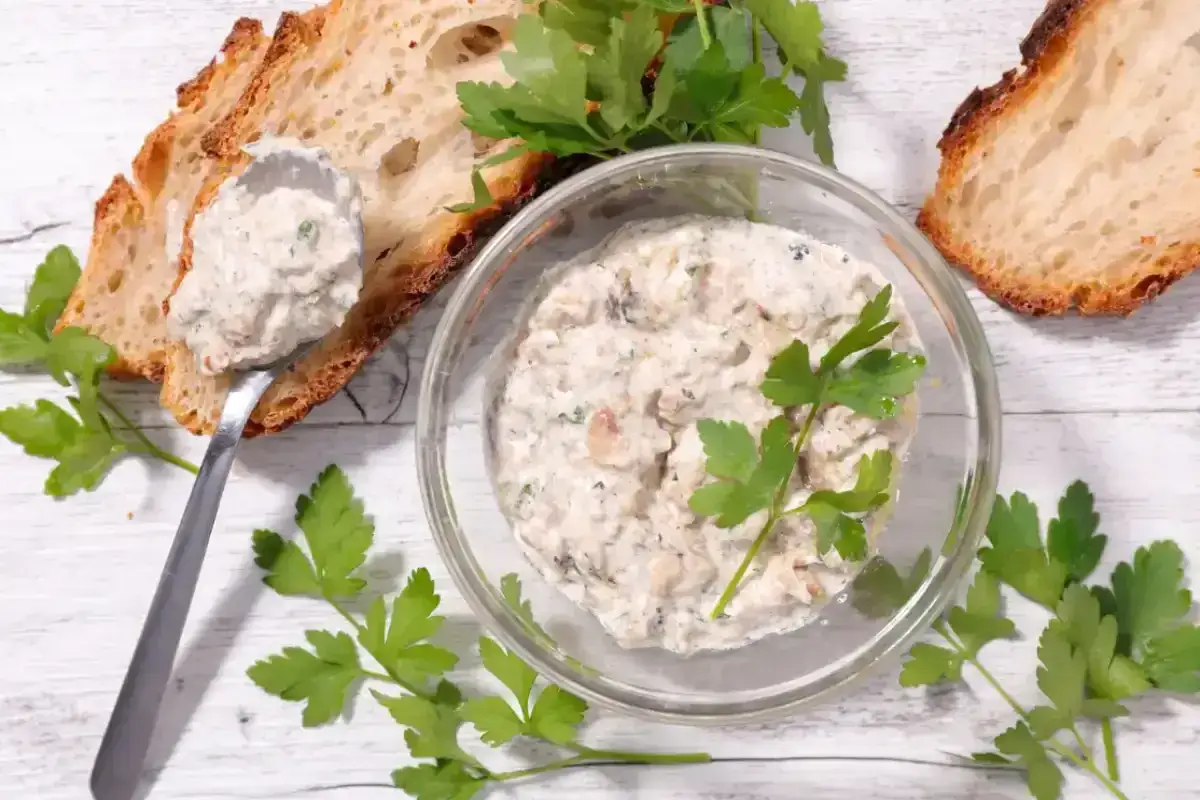Un bol de rillettes de poisson, garni de persil, avec des tranches de pain grill&eacute; et une cuill&egrave;re.
