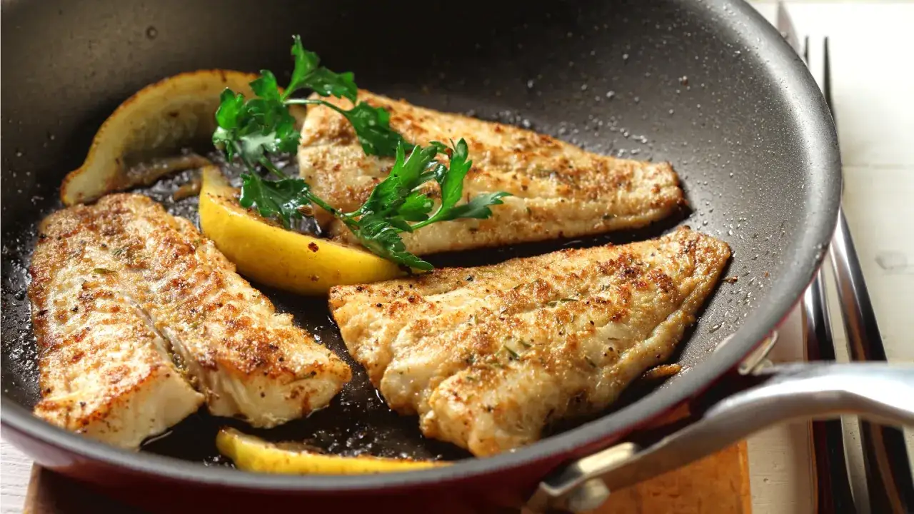 Trois filets de poisson a la poele, dorés et assaisonnés, avec des quartiers de citron et du persil frais.